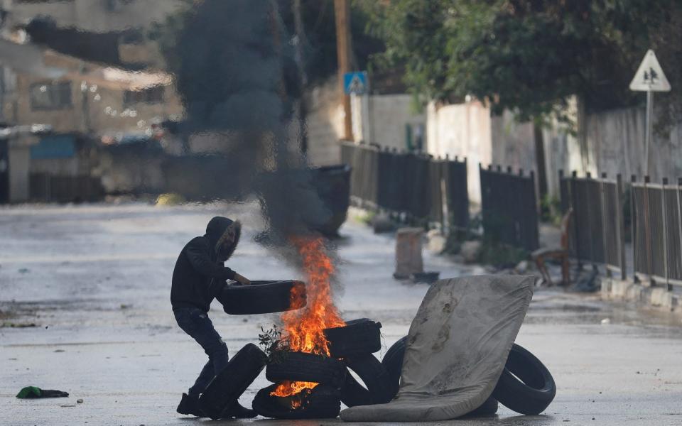Palestinian demonstrator adds a tire to a burning makeshift road block