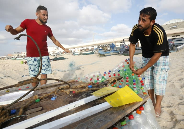 Palestinian fisherman Mouad Abu Zeid (R) fixes his plastic bottle boat on a beach in Rafah in the southern Gaza Strip on August 14, 2018