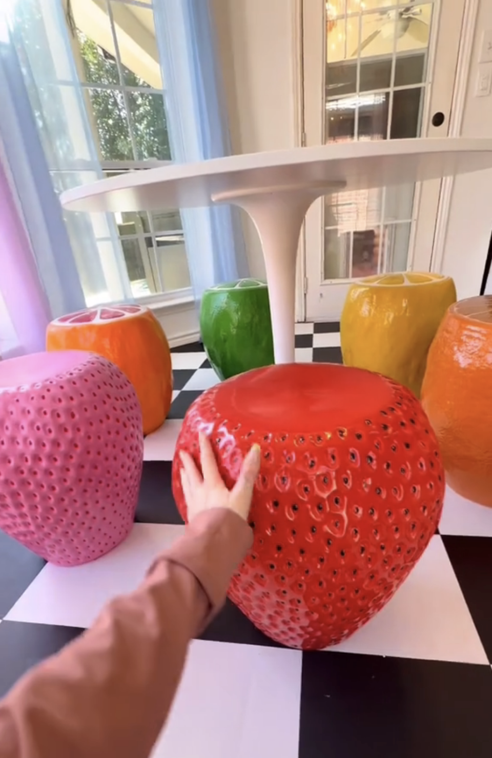 Person touching a large red strawberry chair at the table among the other colorful chair