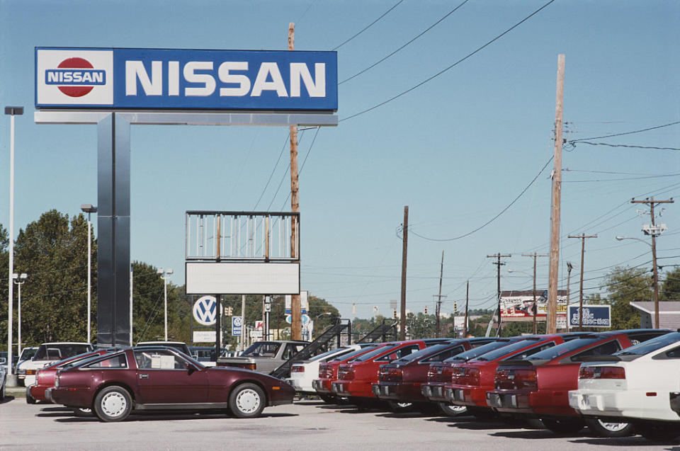 A Nissan car dealership lot with a lineup of vintage cars under a large sign