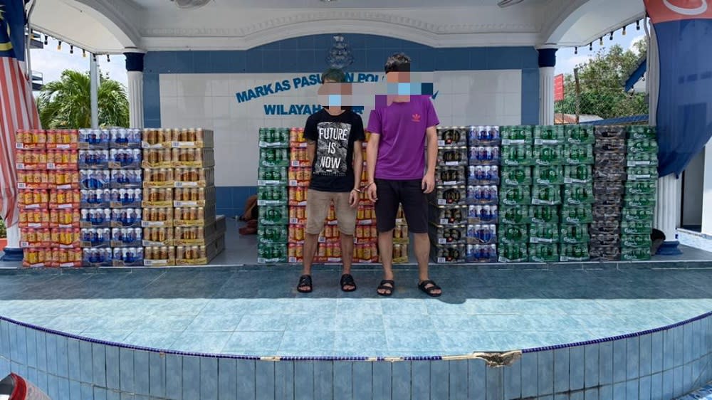 The two suspects with the untaxed alcoholic beverages and liquor at the Region Two Marine Police Force headquarters in Tampoi, Johor Baru. — Picture courtesy of Region Two Marine Police Force