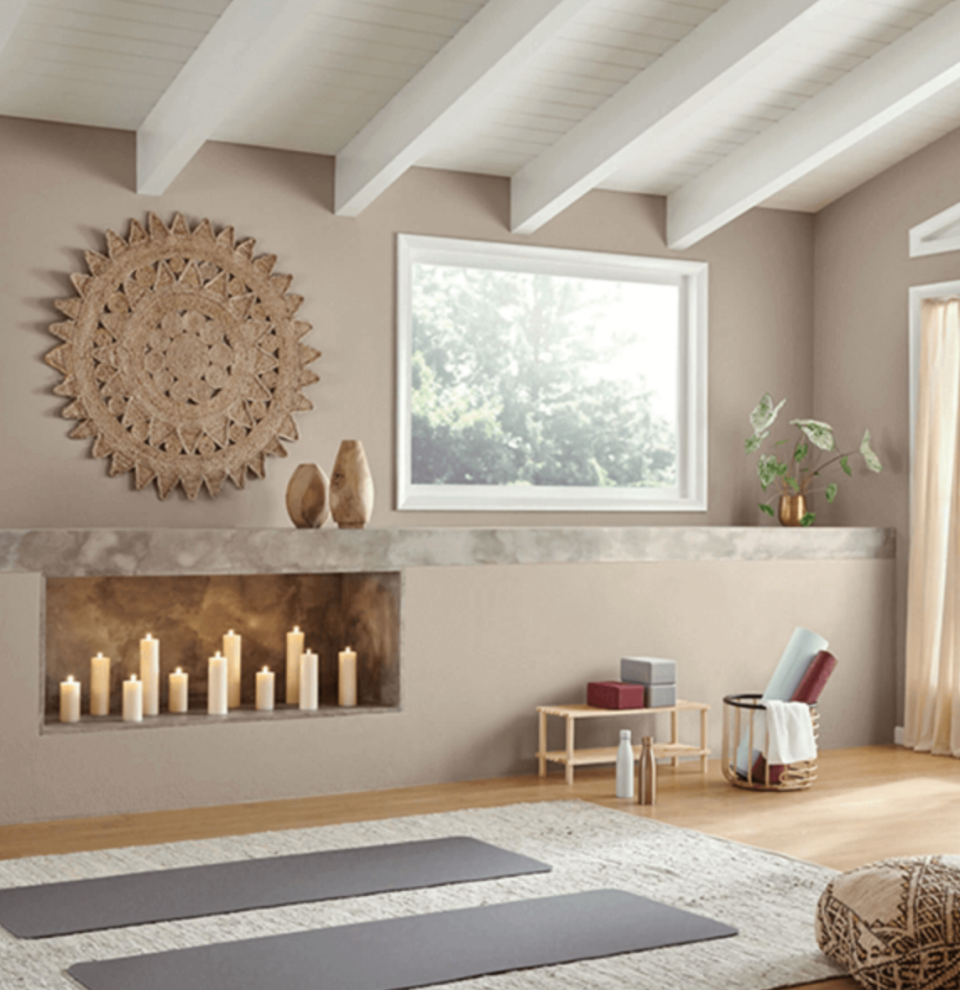 A home yoga studio with candles in an inset shelf and an angled ceiling with warm grey walls and yoga mats set up on the floor