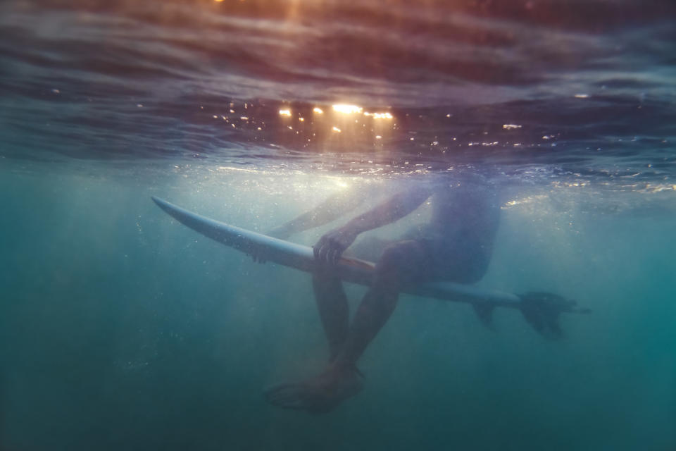View from below the surface of water of a surfer sitting on surfboard