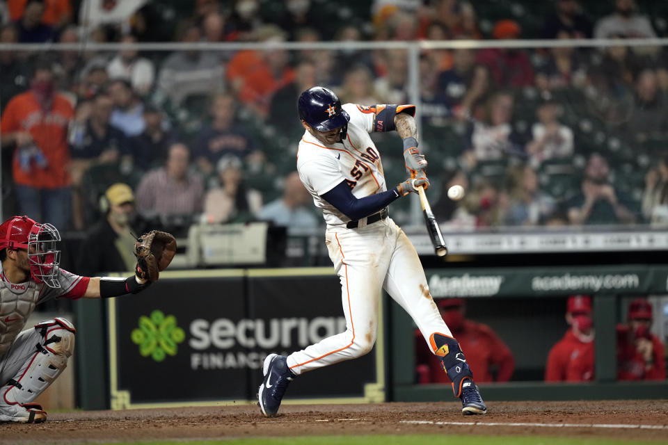 Houston Astros' Carlos Correa, right, hits a RBI single as Los Angeles Angels catcher Kurt Suzuki reaches for the pitch during the third inning of a baseball game Thursday, April 22, 2021, in Houston. (AP Photo/David J. Phillip)