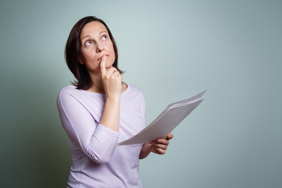 A woman holding paper sheets, looking up and thinking, possibly about lotto numbers.