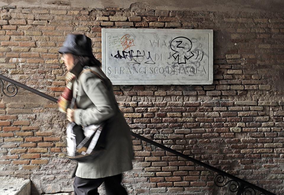 A woman walks past a street name sign scribbled in writings, in Rome, Monday, Nov. 5, 2018. Rome’s monumental problems of garbage and decay exist side-by-side with Eternal City’s glories. (AP Photo/Gregorio Borgia)