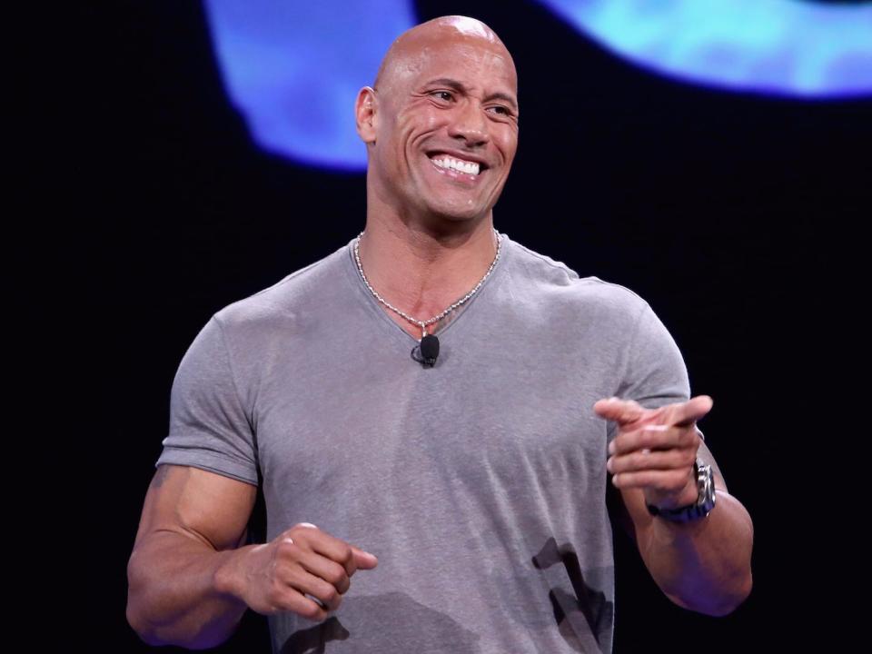 dwayne johnson smiles and points while on stage