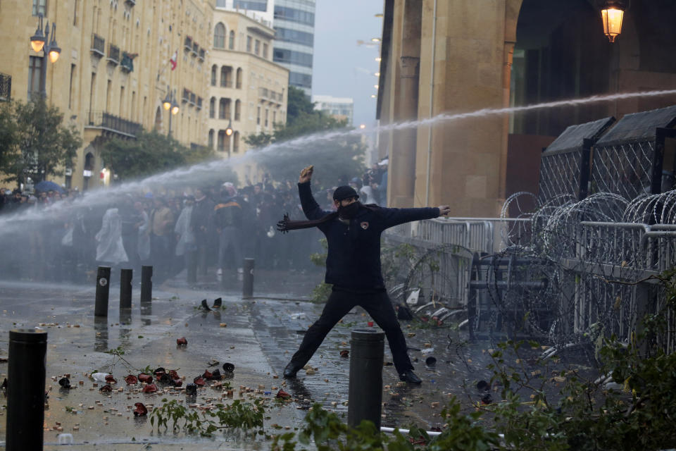 An anti-government demonstrator throws a stone toward riot police at a road leading to the parliament building in Beirut, Lebanon, Saturday, Jan. 18, 2020. Riot police fired tears gas and sprayed protesters with water cannons near parliament building to disperse thousands of people after riots broke out during a march against the ruling elite amid a severe economic crisis. (AP Photo/Hassan Ammar)