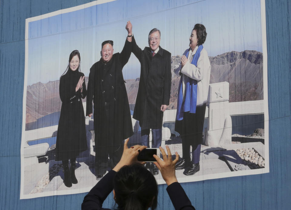 A woman takes a picture of a banner showing a photo of South Korean President Moon Jae-in, second from right, his wife Kim Jung-sook, right, North Korean leader Kim Jong Un and Kim's wife Ri Sol Ju on North Korea's Mount Paektu, at Seoul City Hall in Seoul, South Korea, Tuesday, Oct. 23, 2018. The government of Moon formally approved the rapprochement deals he made with Kim last month. (AP Photo/Ahn Young-joon)