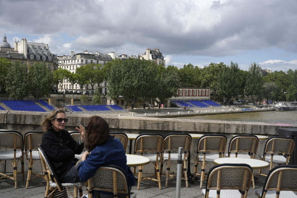 Women discuss by the Seine river with stands installed on its banks, Thursday, July 4, 2024 in Paris. The Seine river will host the Paris Olympic Games opening ceremony on July 26. (AP Photo/Thibault Camus)