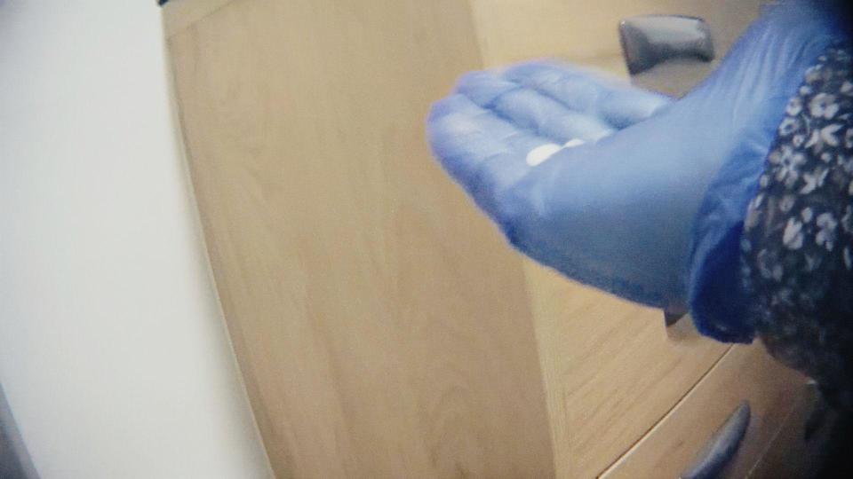 Still from undercover footage showing a hand wearing a blue plastic glove holding some white pills
