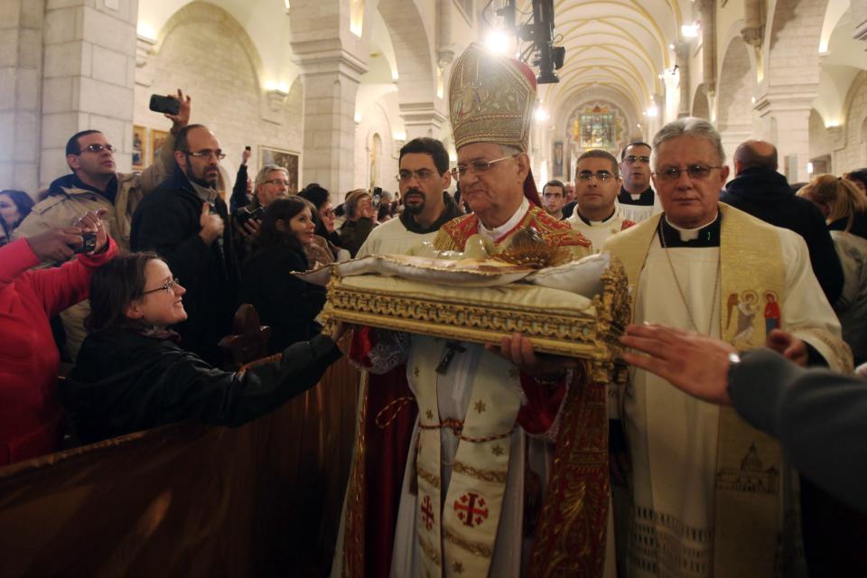 Latin Patriarch of Jerusalem Fouad Twal carries a statuette of baby Jesus during Christmas midnight mass in Bethlehem