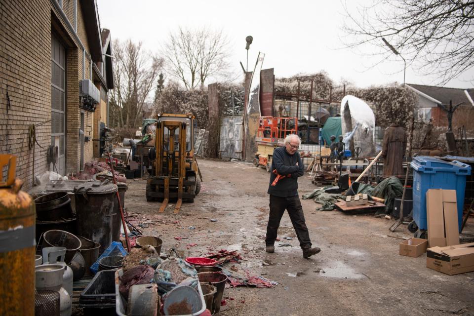 A man bundles up as he walks outside a building surrounded by scrap metals and materials.