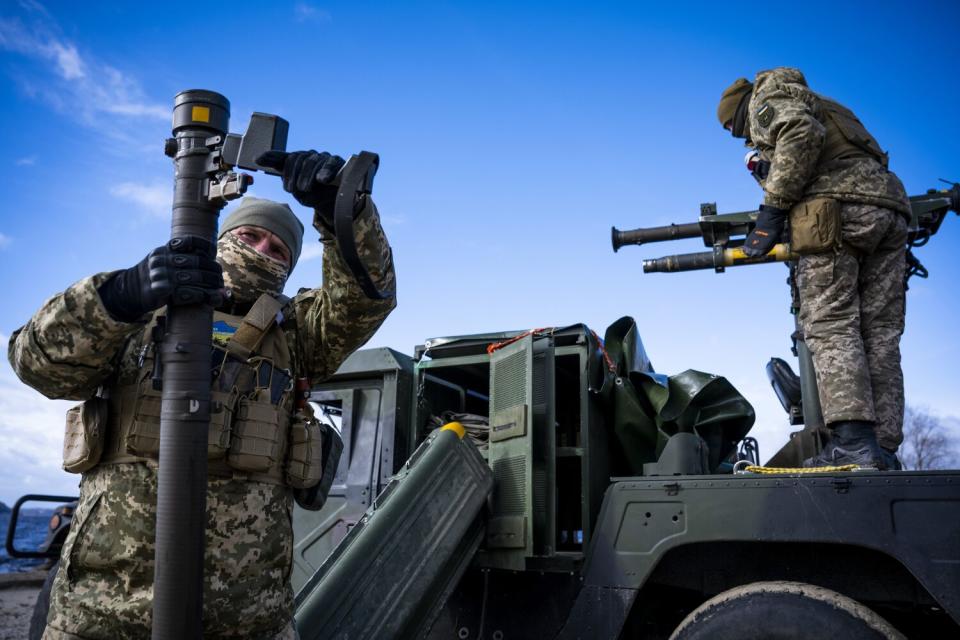 Troops in camouflage fatigues handle a Stinger missile and other heavy arms near a Humvee