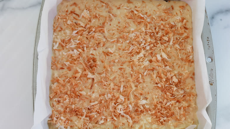 toasted coconut over coconut bar filling in a baking pan