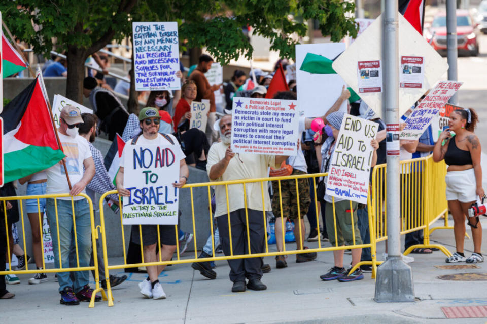 A group of protestors behind metal grates holding signs critical of Israel