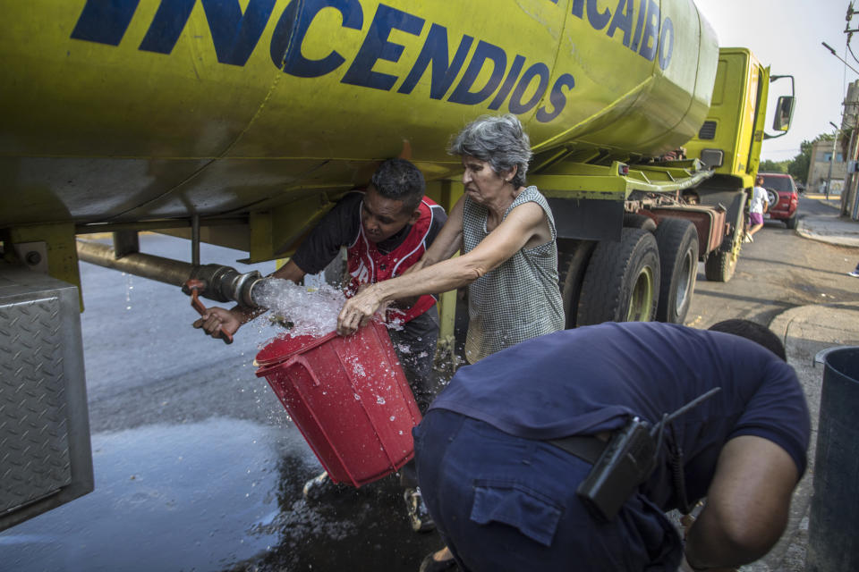 A woman fills a bucket with drinking water from firefighters during water shortages linked to lack of electricity in Maracaibo, Venezuela, May 14, 2019. The opposition blames Venezuela's misery on misguided economic policies, mismanagement and corruption by the socialist administration installed by the late Hugo Chavez. (AP Photo/Rodrigo Abd)