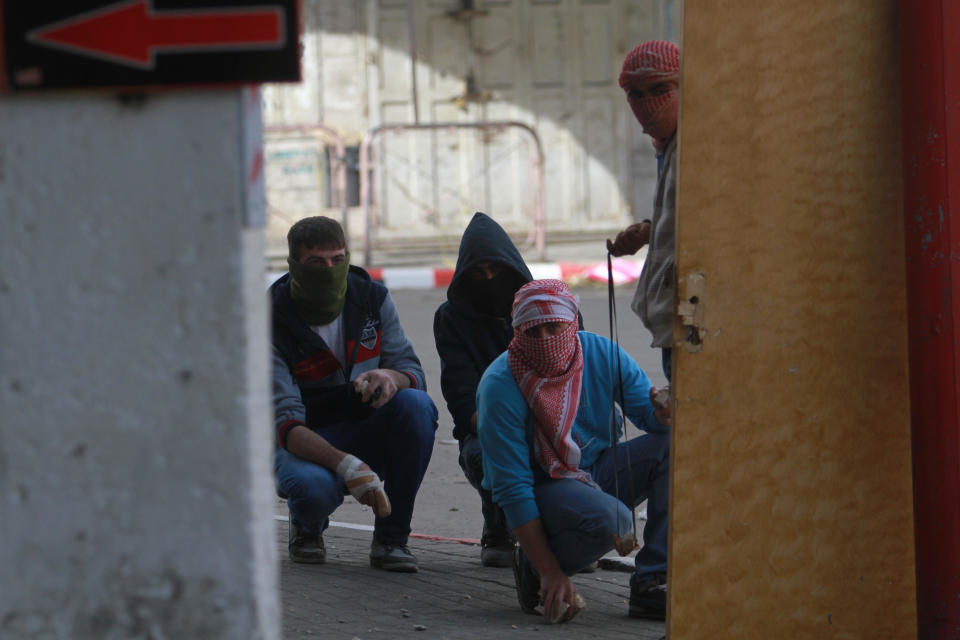 Palestinians take cover from Israeli soldiers in the center of the West Bank city of Hebron, Friday, Feb. 21, 2014, during a demonstration against the closure of the main downtown street. Shuhada street was shut after a 1994 mosque massacre when a settler shot and killed 29 Muslim worshippers. The military closed it citing security reasons. (AP Photo/Nasser Shiyoukhi)