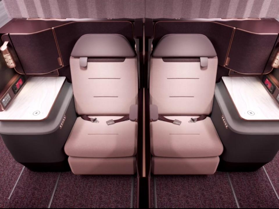 Two pink first class seats side-by-side with armrest and lamps on either side.