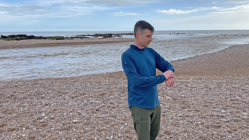 Man on beach wearing Smartwool Men's Active Mesh Hoodie checking watch