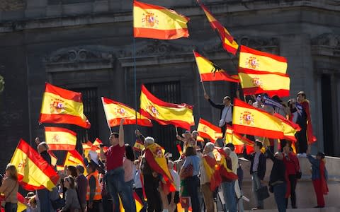 People wave Spanish flags during a mass protest by people angry with Catalonia's declaration of independence - Credit: AP Photo/Paul White