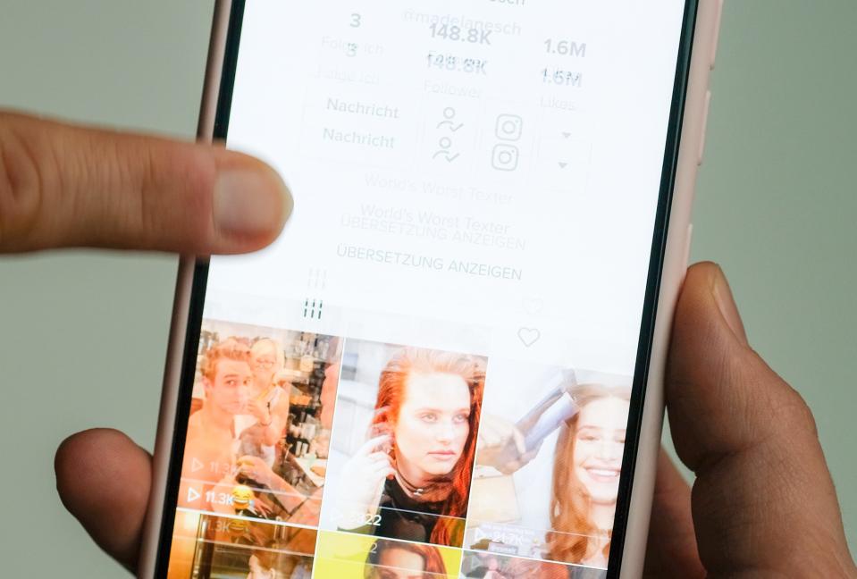 A girl holds her smartphone in her hands on which she has opened @madelainepetsch's profile in the short video app TikTok.