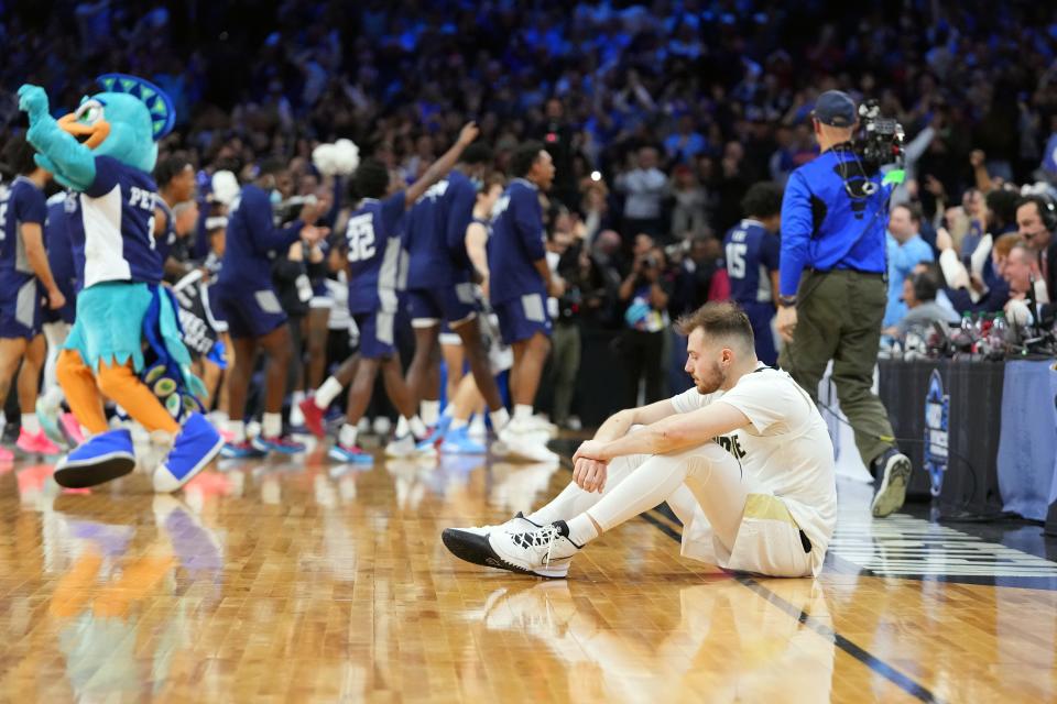 Purdue guard Sasha Stefanovic sits on the court as Saint Peter's celebrates behind him after the Peacocks upset the Boilermakers in the Sweet 16.