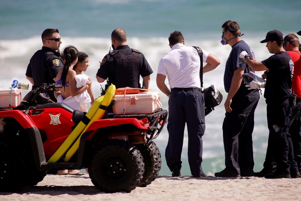 Palm Beach fire rescue workers and Palm Beach police officers speak with three sisters who got caught in a rip current at Midtown Beach in February. Two sisters were rescued while a third made it back to shore on her own.