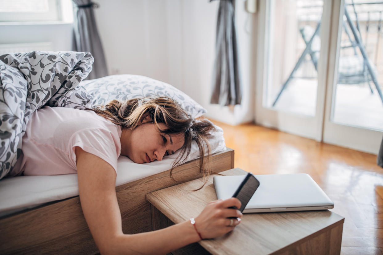 Young woman is waking up and looking at her smart phone. bed rotting