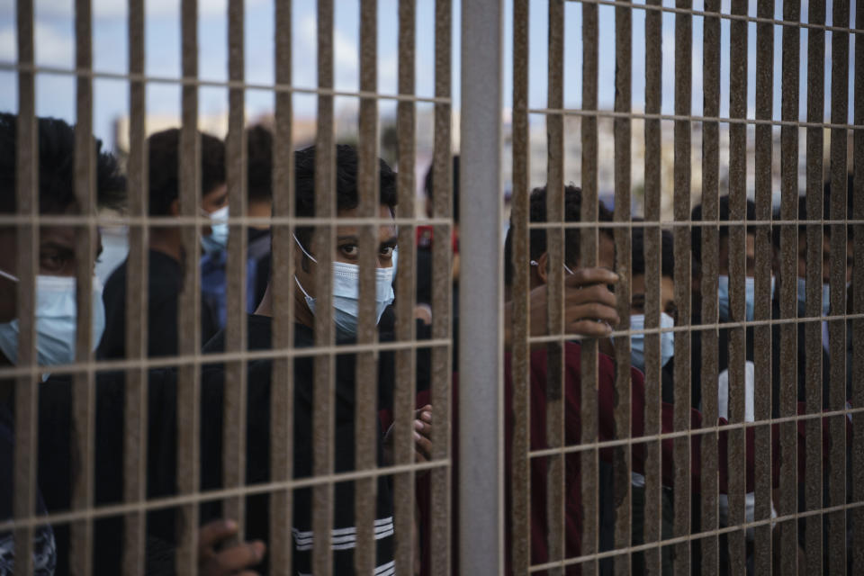 Migrants who crossed the Mediterranean Sea by boat line up behind a fence in Lampedusa, Italy, Friday, Oct. 1, 2021, as they wait to board a ferry to Sicily. Despite the risks, many migrants and refugees say they'd rather die trying to cross to Europe than be returned to Libya where, upon disembarkation, they are placed in detention centers and often subjected to relentless abuse. (AP Photo/Renata Brito)