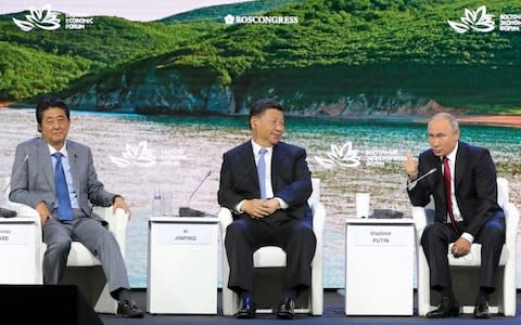 Vladimir Putin speaks at a forum in Vladivostok with Shinzo Abe, left, and Xi Jinping - Credit: The Asahi Shimbun via Getty Images