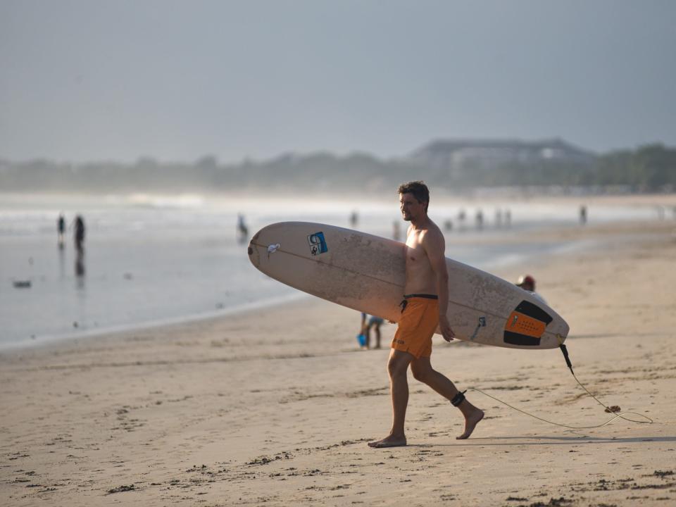 a man walks with a surfboard across a beach in bali