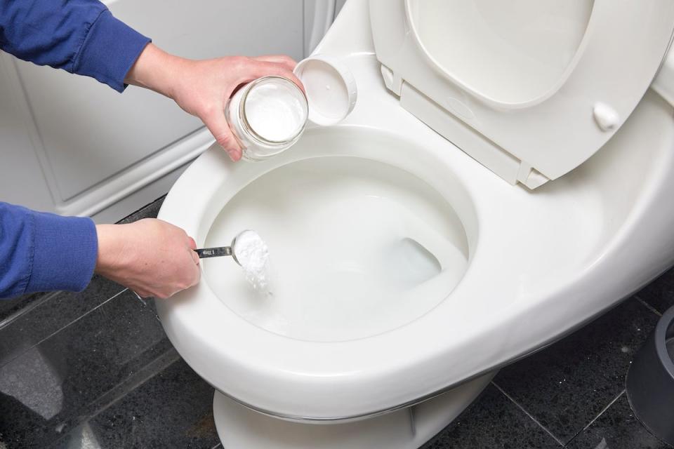 Woman scoops homemade toilet bowl cleaner into the toilet bowl. 