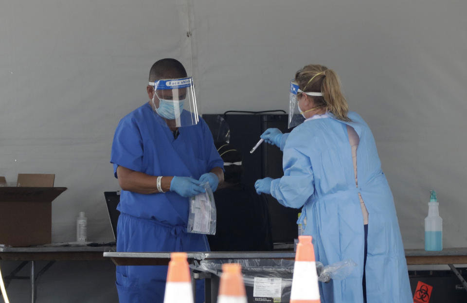 Healthcare workers put a vial containing a test swab into a bag after testing a driver at a drive-through coronavirus testing site outside of Hard Rock Stadium, Friday, June 26, 2020, in Miami Gardens, Fla. Florida banned alcohol consumption at its bars Friday as its daily confirmed coronavirus cases neared 9,000, a new record that is almost double the previous mark set just two days ago. (AP Photo/Wilfredo Lee)