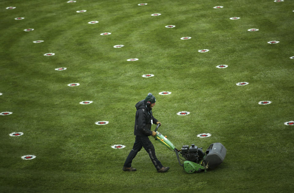 A member of the grounds staff cuts the grass dotted with social distance markers in the parade ring before the start of the Liverpool NHS Day of the 2021 Grand National Festival at Aintree Racecourse in Liverpool, England, Thursday April 8, 2021. The Aintree Grand National 2021 is a the three day festival of horse racing first run in 1839.(Tim Goode/PA via AP)