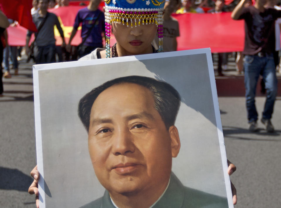 In this photo taken on Sunday, Sept. 16, 2012, a female demonstrator dressed in a traditional costume holds a picture of the late Communist leader Mao Zedong while marching with others during an anti-Japan protest outside the Japanese Embassy in Beijing. The face of dissatisfaction with China’s Communist Party is the face of the man synonymous with it: Mao Zedong. Portraits of the revolutionary leader, hoisted by people born after his death 36 years ago, often led packs of demonstrators in protests over Japan’s effort last week to bolster its hold on islands claimed by China. (AP Photo/Andy Wong)