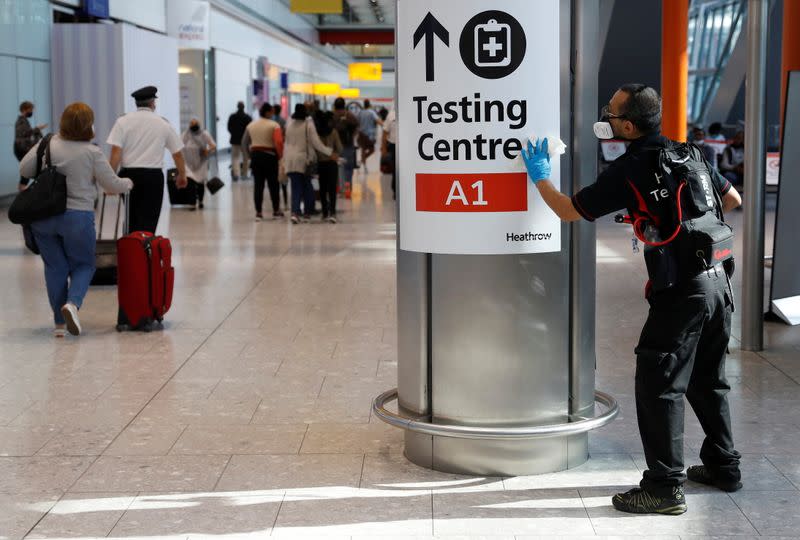 FILE PHOTO: A worker sanitises a sign at the International arrivals area of Terminal 5 in London's Heathrow Airport