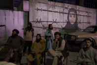 Taliban members sit in front of a mural depicting a woman behind barbed wire in Kabul, Afghanistan, Tuesday, Sept. 21, 2021. (AP Photo/Felipe Dana)