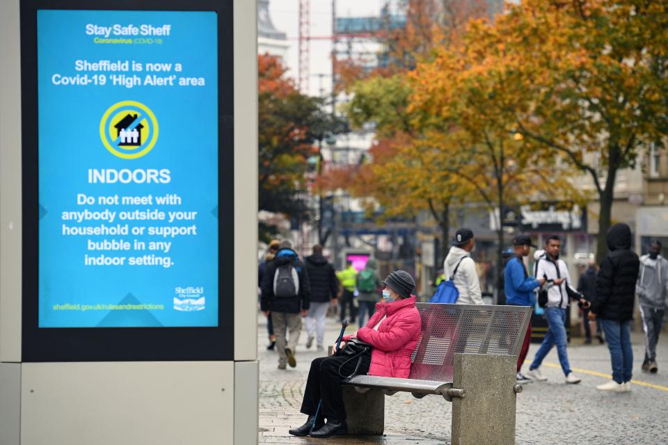 A woman wearing a face mask or covering due to the COVID-19 pandemic, sits on a bench close to a display showing health advice in the shopping district in central Sheffield, south Yorkshire on October 21, 2020, prior to further lockdown measures as the number of novel coronavirus COVID-19 cases rises. - More than a million people in northern England will be banned from mixing with other households under tougher new coronavirus rules announced by government minister Robert Jenrick on Wednesday.  The county of South Yorkshire, which includes the city of Sheffield, will enter into "very high alert" restrictions from 12.01am on Saturday (2301 Friday GMT). (Photo by Oli SCARFF / AFP) (Photo by OLI SCARFF/AFP via Getty Images)