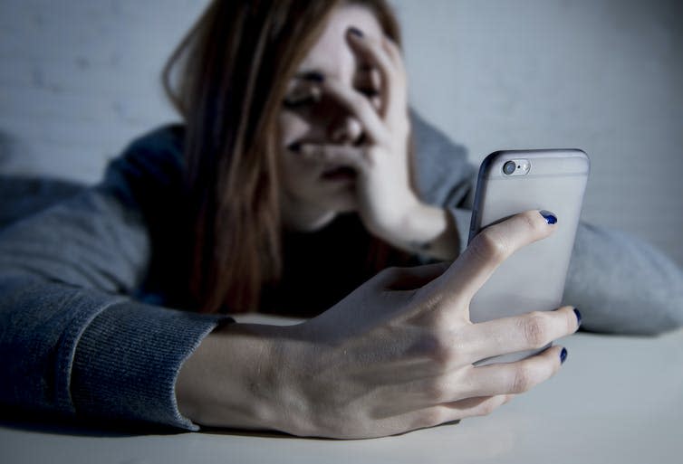 A young woman holding a mobile phone covers her face with her hand