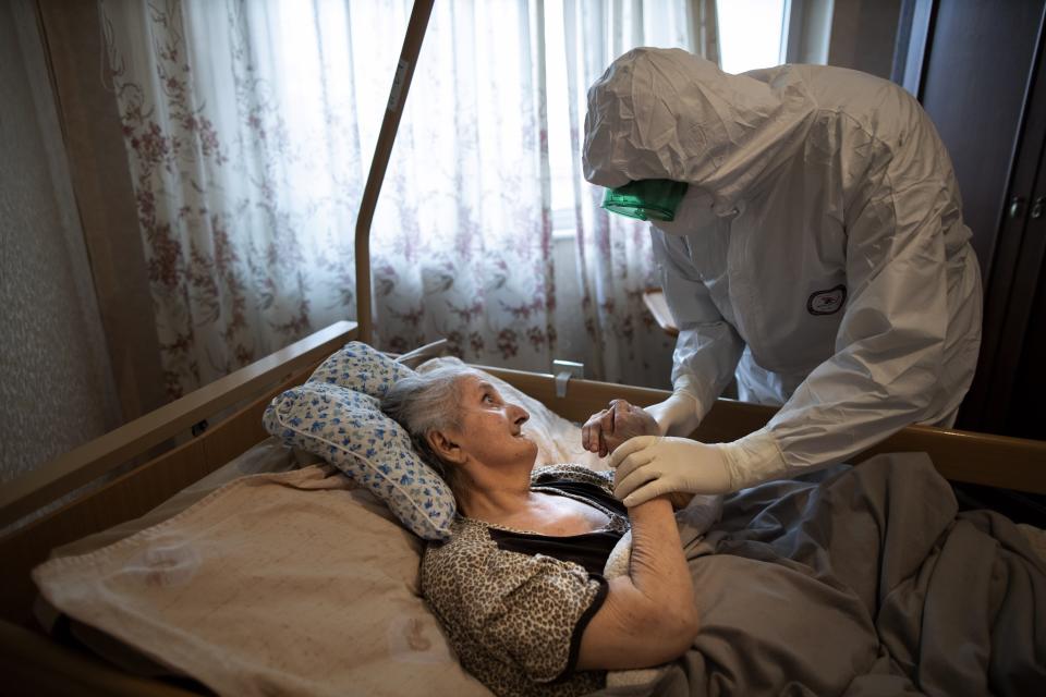 In this photo taken on Monday, June 1, 2020, Father Vasily Gelevan, wearing a biohazard suit and gloves to protect against the coronavirus, speaks to Lyudmila Polyak, 86, who is suspected of being infected with the coronavirus, at her apartment in Moscow, Russia. In addition to his regular duties as a Russian Orthodox priest, Father Vasily visits people infected with COVID-19 at their homes and hospitals. (AP Photo/Alexander Zemlianichenko)