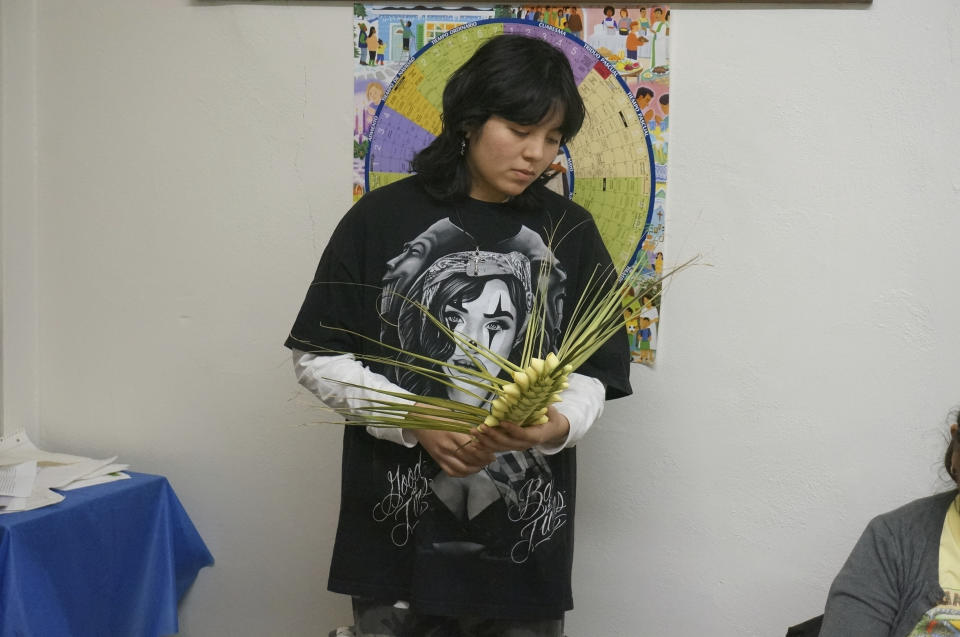 Jahydi Sanchez waits for more instructions to weave a palm frond at the Church of the Incarnation in Minneapolis on Wednesday, March 29, 2023. Love for crafts drove the high school junior to attend the workshop at the Catholic church, where volunteers gathered to weave the palms that will be sold as a fundraiser and blessed at Palm Sunday services this weekend. (AP Photo/Giovanna Dell’Orto)