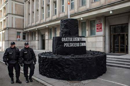 Police officers walk as the Greenpeace activists demonstrate on a street following the decision of the Court of Justice of the European Union (CJEU), after the demonstrators handed a big, carbon cake to Poland's Energy Mister Krzysztof Tchorzewski as a symbol of 'protecting Polish smog', in Warsaw, Poland February 22, 2018. The sign reads: 'We congratulate the defense of Polish smog'. Agencja Gazeta/Dawid Zuchowicz via REUTERS