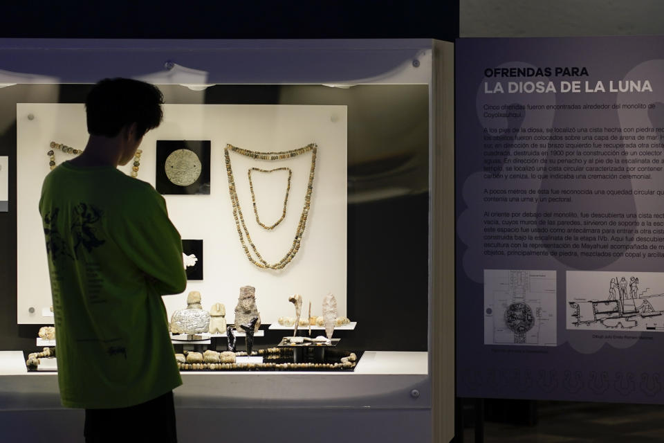 A visitor looks at offerings for the Mexica lunar goddess Coyolxauhqui discovered in the ruins of the Templo Mayor in 1978, on exhibit at the Museum of Templo Mayor in Mexico City, Wednesday, March 29, 2023. The exhibit marks the 45th anniversary of the discovery of a monolith depicting Coyolxauhqui, the Mexica lunar goddess. (AP Photo/Eduardo Verdugo)