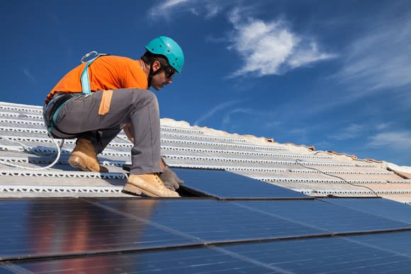 A worker installing solar panels on a rooftop.
