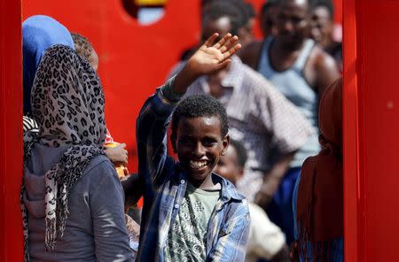 A child waves as other migrants wait to disembark from a merchant ship in the Sicilian harbour of Pozzallo, Italy August 2, 2015. REUTERS/Antonio Parrinello