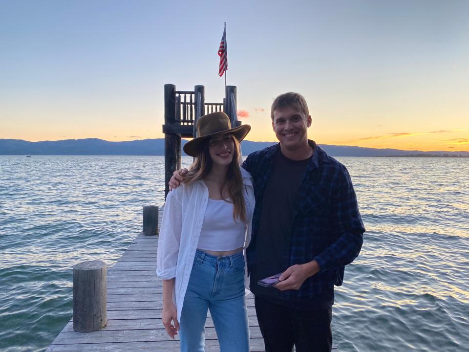 Two adults embracing for a picture on a dock on a lake at sunset.