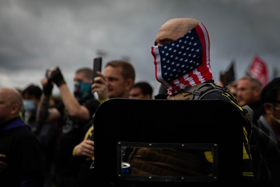 A man in a U.S. flag mask and carrying a riot shield holds his hand to his heart