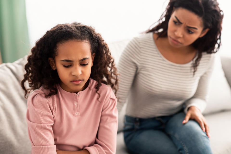 Family Misunderstanding, Childhood Problems. Sad offended black daughter sitting on the couch, turning back to mother after quarrel at home, upset woman asking resentful girl what's wrong