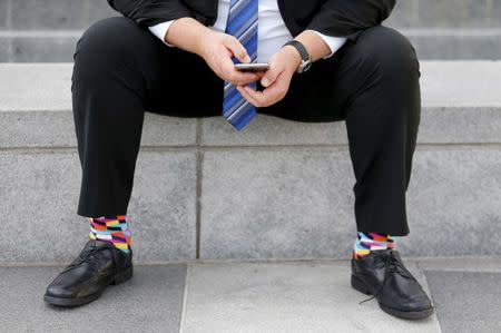 A businessman sits on a bench looking over his mobile phone in downtown San Francisco, California February 4, 2016. REUTERS/Mike Blake